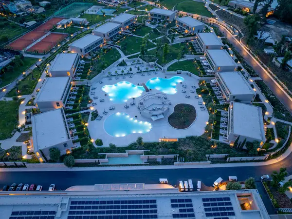 Alacakaranlıkta, havuz, villa, tenis kortu, manikürlü manzara ve güneş panellerini vurgulayan savurgan bir tatil beldesini görüntüler..