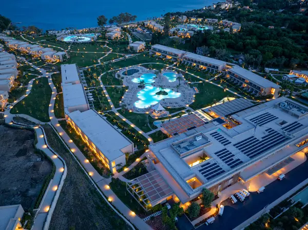 Alacakaranlıkta lüks bir tatil köyünü gösteren havuz, patikalar, modern binalar ve kıyı şeridindeki bereketli peyzajlar.