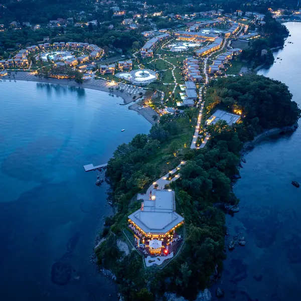 Bir hava görüntüsü, akşam karanlığında aydınlanan ve bereketli manzaralar ve sakin sularla bezenmiş pitoresk bir sahil şeridi boyunca uzanan bir sahil beldesi yakalar..