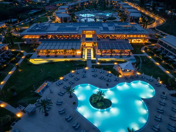 Alacakaranlıkta lüks bir tatil köyü manzarası büyük bir havuz, modern mimari tasarım, manzara ve geniş bir açık hava aydınlatması içerir..