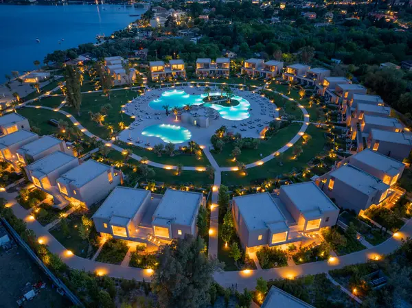 Gece hava manzarası, manzaralı ve huzurlu bir ortam için aydınlatılmış büyük, davetkar bir havuz alanını çevreleyen modern villaların yer aldığı lüks bir tatil köyü sergiliyor..