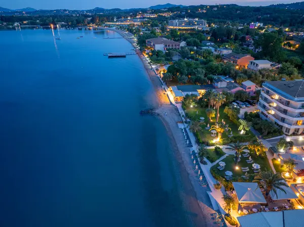 Bir hava görüntüsü, gece vakti aydınlık binalarla dolu bir sahil şeridini su kenarında hareketli bir sahne oluşturur, sakin bir akşam atmosferi..