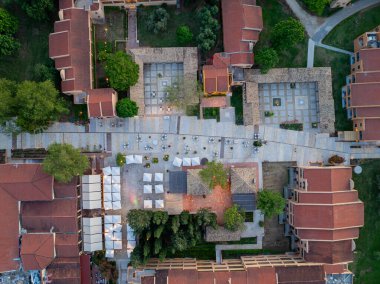 Kırmızı çatılı geleneksel binaların yer aldığı, avlularla, kaldırımlarla ve ağaçlarla birbirine bağlandığı kentsel bir açık hava alanının genel görüntüsü..