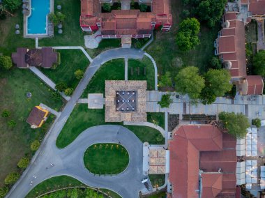 Zarif bir tatil köyünün yukarıdan çekimi. Havuz, kırmızı çatılı binalar, yeşil çimenler, ağaçlar ve dolambaçlı yollar. Akşam ışıltısı hediyesi.