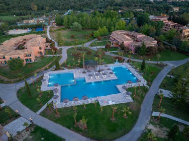 Etrafı şezlonglar, bahçeler ve büyüleyici konaklama yerleriyle çevrili çok bölümlü bir yüzme havuzunun yer aldığı geniş bir tatil köyünün genel görüntüsü..