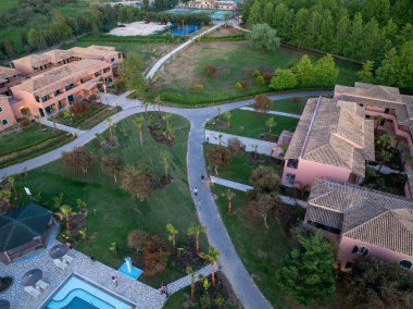 Genel bakış açısı, birden fazla bina, yeşil alanlar boyunca kıvrılan yollar ve ferahlatıcı bir havuz alanı olan sakin bir tatil köyü ayarını yakalar..