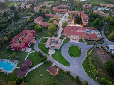Havadan çekilen görüntülerde kırmızı çatılı binalar, yeşil çimenler ve ağaçlarla kaplı geniş bir tatil köyü görülüyor. Arazide bir havuz ve manikürlü manzara da yer alıyor..