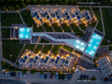 Yukardan aşağıya doğru çekilen bir çekim, parlak havuzları ve modern mimarisi olan, yemyeşil peyzaj ve çevre aydınlatmasıyla bezenmiş şık bir tatil beldesi yakalıyor..