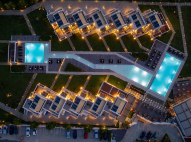 Yüksek açılı çekimler, villaları, havuzları, peyzajı, güverteleri ve otoparkı olan bir tatil köyünü gece aydınlatıyor. Lüks bir kaçış yeri..