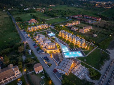 Havadan bakıldığında, birçok yüzme havuzu, villaları, bahçeleri ve akşam saatlerinde bir plaj alanı olan aydınlık bir tatil köyü görülüyor..