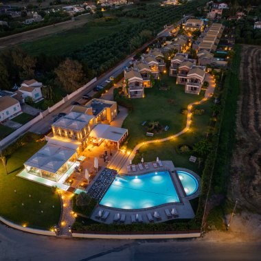 Parlak bir havuz, patikalar ve konaklama yeri olan bir tatil köyünün havadan çekilmiş görüntüsü. Alacakaranlıkta bir alana yaslandığında, sahne huzur yayar..