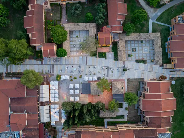 Kırmızı çatılı geleneksel binaların yer aldığı, avlularla, kaldırımlarla ve ağaçlarla birbirine bağlandığı kentsel bir açık hava alanının genel görüntüsü..