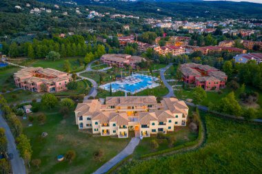 Merkez havuzu çevreleyen çeşitli binaların bulunduğu geniş bir tatil köyünün tepeden görünüşü akşam ışığında yeşillik ve uzak dağlarla tamamlanmış..