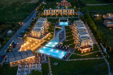 Alacakaranlıkta lüks bir tatil köyünün havadan görünüşü. Villalar çoklu yüzme havuzlarının etrafını sarar, sakin ve davetkar bir tatil yeri yaratırlar..