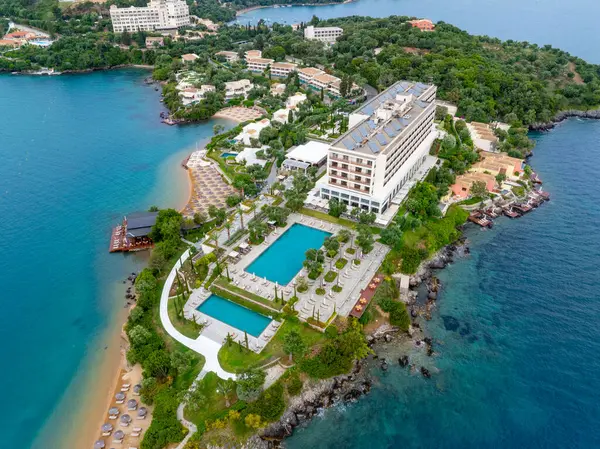 Plajı, yüzme havuzları ve deniz kenarındaki yemyeşil bir araziye kurulmuş binaları olan bir tatil köyünün havadan görünüşü rahatlatıcı..