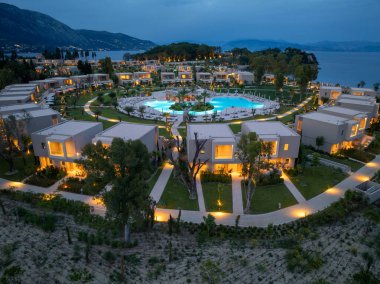 Bu hava görüntülerinde çağdaş binalar, merkez havuz alanı ve alacakaranlıkta bir sahile sahip iyi tasarlanmış bir tatil köyü sergileniyor..