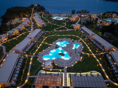 Günbatımında savurgan bir tatil köyü, parlak havuzlar, dolambaçlı yollar ve bitişik okyanus manzarasıyla tepeden çekimler sergiliyor.. 