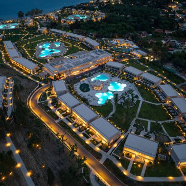 Gece vakti hava gösterileri, yeşil alanlar ve kıyıları çevreleyen ışıklı havuzları, yolları ve villaları olan modern bir tatil köyü tesisi..