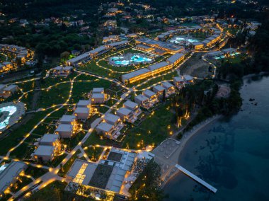 Gece vakti aydınlık villaları, havuzları ve yolları olan bir tatil köyünün havadan görünüşü. Sahile ve okyanusun kenarına yerleştirilmiş..