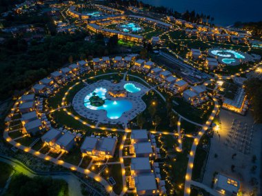 Hava gece görüşü, havuz, patika ve konaklama binaları olan bir tatil köyü gösteriyor. Hepsi de stratejik olarak yerleştirilmiş ışıklandırmayla geliştirilmiş..