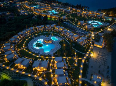 Çok güzel aydınlatılmış bir tatil köyünün gece çekimleri lüks konaklamalar, yüzme havuzları ve karanlık gökyüzüne karşı manikürlü çimenler..