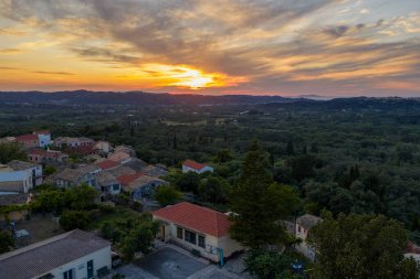 Resimli bir kasaba, batan güneşle güzelce aydınlatılan yeşil bir arazinin ortasında, sakin manzaranın üzerine altın bir parıltı saçıyor..