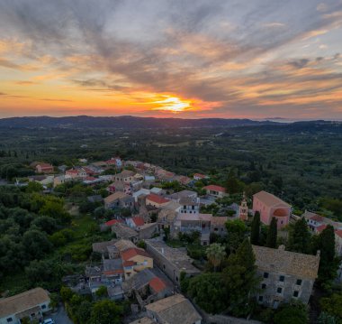 Yoğun ağaçlarla çevrili, batan güneşin sıcacık parıltısıyla yıkanmış, kırmızı çatılı binaları olan sakin bir köy. Yumuşak bulutlu Ufuk.