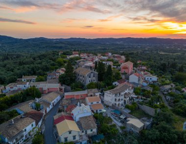 Alacakaranlıkta cennet gibi bir köy manzarası başlıyor. Renkli çatıları olan taş binalar canlı bulutlu gökyüzünün altında yeşil tepelerde duruyor..