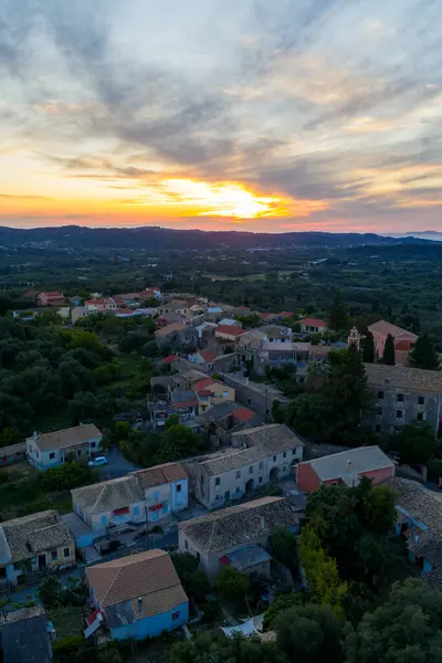 Bu hava çekimi, doğa ve mimarinin barışçıl bir karışımını sergileyen, dramatik bir günbatımına karşı evleri ve ağaçları olan sakin bir köyü yakalar..