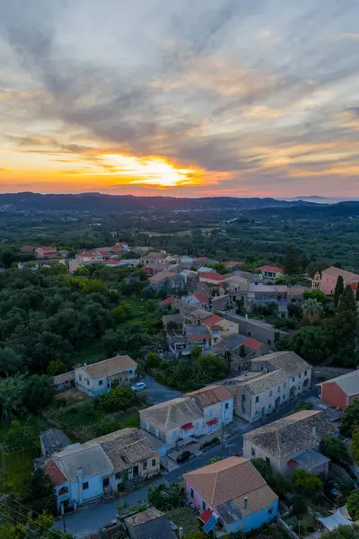 Ağaçların arasında renkli evleri olan büyüleyici bir köyün havadan görünüşü. Canlı bir günbatımı gökyüzünü boyar, huzurlu bir atmosfer yaratır..
