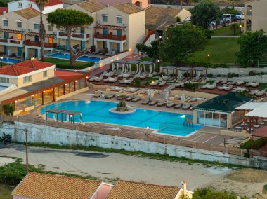 Bu resim birkaç havuz, güneşlik, ağaçlar ve binalarla lüks bir tatil köyü yakalıyor. Güzel, rahatlatıcı, tatil ortamı yaratıyor..