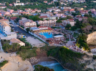 Yüksek açılı perspektif, tatil köyü binaları ve havuzu olan dramatik kaya oluşumları ve küçük bir plaj oluşumunun yanında tünemiş bir sahil kasabasını gözler önüne seriyor..