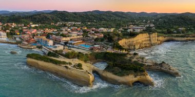 Alacakaranlıkta, kumlu uçurumlar, berrak sular ve yemyeşil tepeler tarafından desteklenen canlı binalarla bir kıyı köyünü görüntüler..