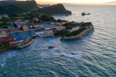 Yüksek bir manzara gün batımında bir sahil köyünü yakalar. Otel binaları uçurumun kenarına tünemiş, turkuaz deniz manzaralı..