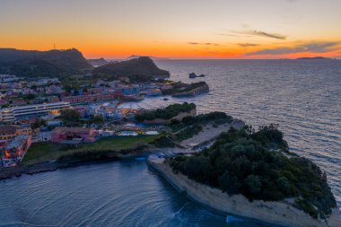 Canlı bir günbatımında, eşsiz kaya oluşumları, berrak su ve güzel bir gökyüzü altında uzak dağları barındıran bir sahil köyünün havadan görünüşü..