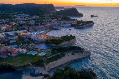 Manzaralı hava manzarası, oteller, evler, uçurumlar ve okyanus kıyısındaki canlı günbatımı gökyüzünün yer aldığı Akdeniz 'de yaşayan kıyı manzarasını yakalıyor..