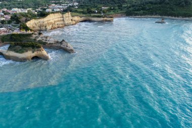 Dramatik uçurumlar ve canlı turkuaz suların yer aldığı bir kıyı şeridine ait hava perspektifi, karanın ve denizin görkemli uyumunu vurguluyor..