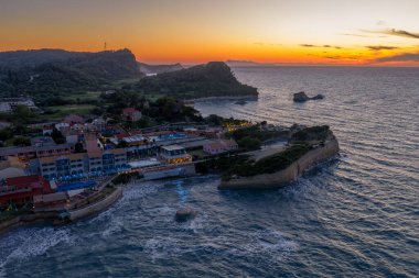 Gün batımında deniz kıyısında binalar, uçurumlar ve okyanus dalgaları olan renkli bir gece gökyüzü altında bir köyün havadan görünüşü..