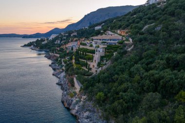Uçuruma bakan bir tepedeki lüks villa kompleksi. Etrafı yemyeşil yemyeşil dağlarla çevrili. Akşam gökyüzünün altında dağlar var..