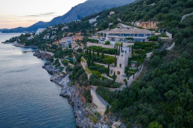 Geniş bir villa, dingin bir okyanusa bakan gür, kayalık bir kayalık yamacın üzerinde, alacakaranlık ya da şafağın yumuşak ışığında yıkanır.. 