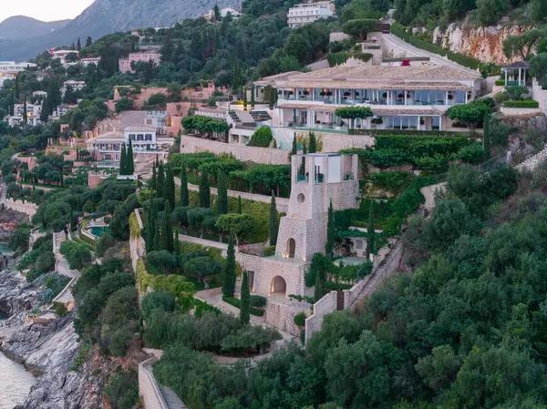 Yeşil bir tepenin üzerinde uzanan geniş bir malikane, taş bir kule, manzaralı teraslar ve görkemli deniz manzarası sunuyor..