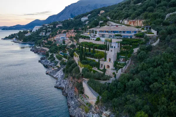 Geniş bir villa, dingin bir okyanusa bakan gür, kayalık bir kayalık yamacın üzerinde, alacakaranlık ya da şafağın yumuşak ışığında yıkanır.. 