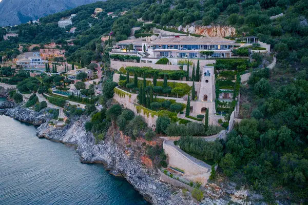 Varlıklı bir villa, denize bakan kayalık bir uçurumun tepesine tünemiş. Yamaç boyunca uzanan yemyeşil bahçeler suya çıkıyor..