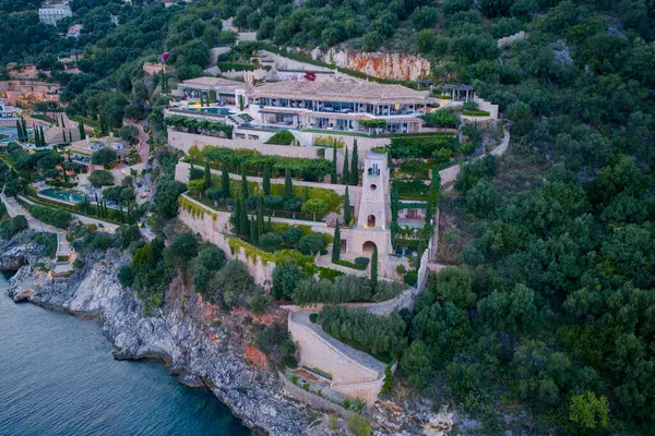 Bu resim, mimariyle doğayı harmanlayan bir uçurumun kenarındaki geniş bir malikaneyi gösteriyor. Peyzajlı bahçeler ve okyanus manzarası dingin bir zemin oluşturur.