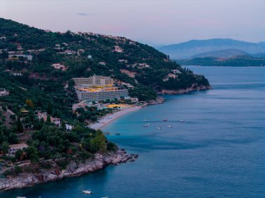 Tepedeki bir tatil köyünün akşam manzarası, teknelerle benekli sakin bir koy. Alacakaranlık gökyüzü, manzaranın ve suyun üzerine mavi bir renk salıyor..