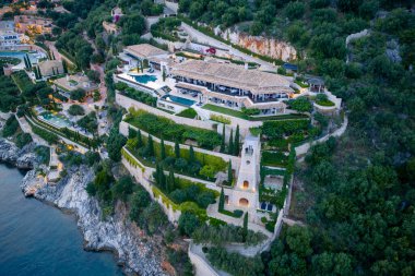 Kıyı boyunca uzanan birden fazla bina, havuz ve bereketli teras bahçelerinin yer aldığı geniş bir yamaç arazisini hava manzarası yakalıyor..