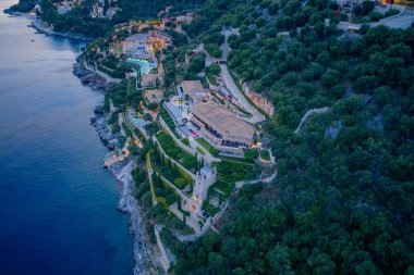 Geniş bir sahil villası, alacakaranlıkta aydınlanan, yemyeşil Akdeniz 'in ortasında, aşağıdaki gök mavisi suların çarpıcı manzarasını sunar..