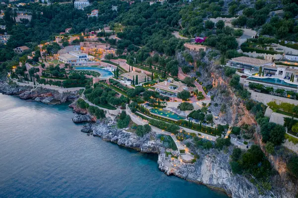 Lüks bir sahil beldesini gösteren hava manzarası sakin bir akşamda sakin, mavi deniz manzaralı yeşil bir yamaca kusursuz bir şekilde entegre edilmiştir..