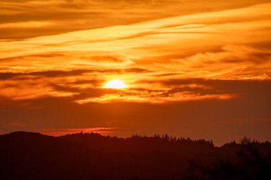 Canlı bir günbatımı ufku bulutlar ve tepelerle aydınlatacak, doğada güzel ve sakin bir ortam yaratacak..