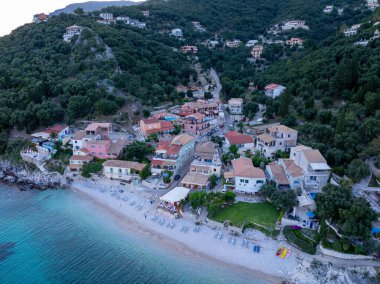 Çakıl taşı plajı ve bereketli tepelerin yakınındaki renkli binaların bulunduğu bir sahil köyünün tepeden görünüşü. Huzurlu sahne rahatlama çağrıştırıyor.
